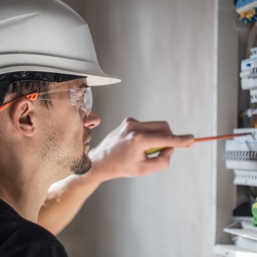 man, an electrical technician working in a switchboard with fuses. Installation and connection of electrical equipment. Close up. Man, an electrical technician working in a switchboard with fuses. Installation and connection of electrical equipment. Professional with tools in hand. concept of complex work, space for text.
