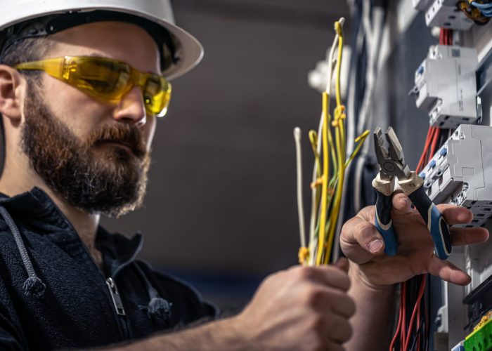 A male electrician works in a switchboard with an electrical connecting cable. A male electrician works in a switchboard with an electrical connecting cable, connects the equipment with tools.
